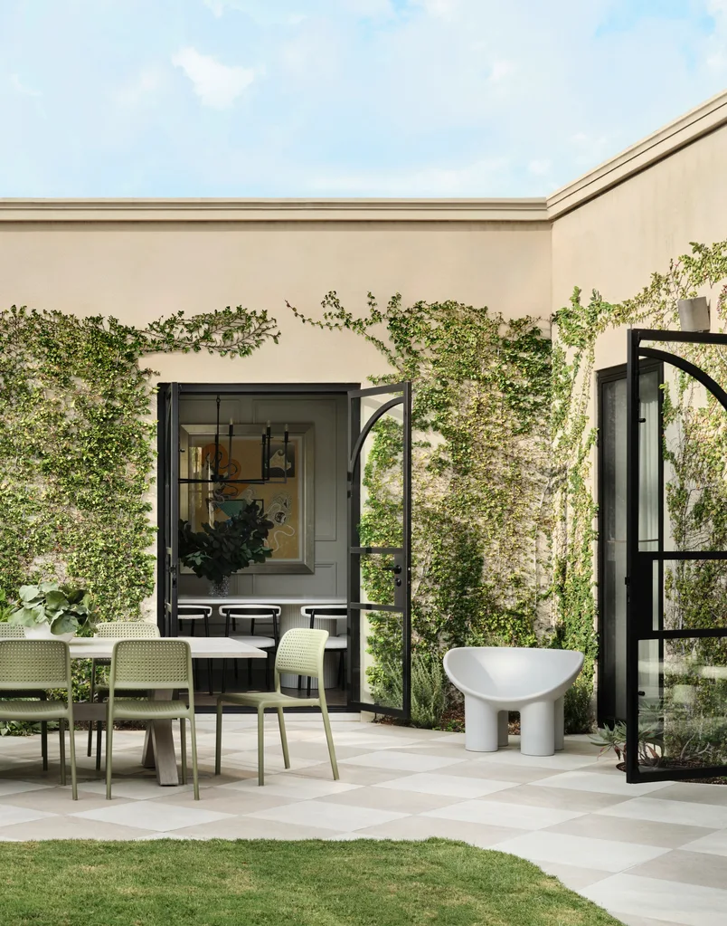 Outdoor patio with green chairs, table, white chair, open glass doors, and walls covered in green ivy.