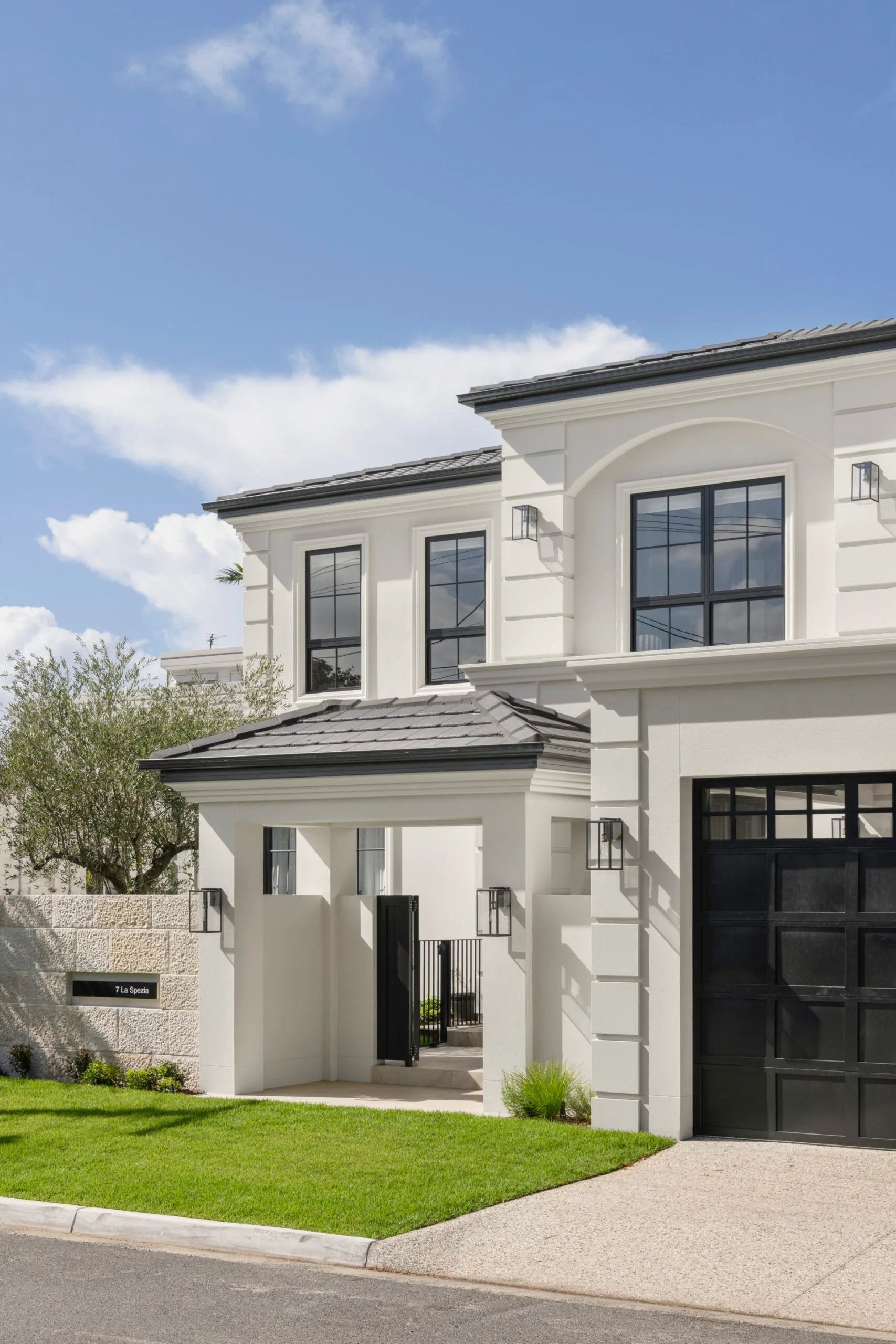 Elegant modern white house with black framed windows and a neatly landscaped front yard under a clear blue sky.