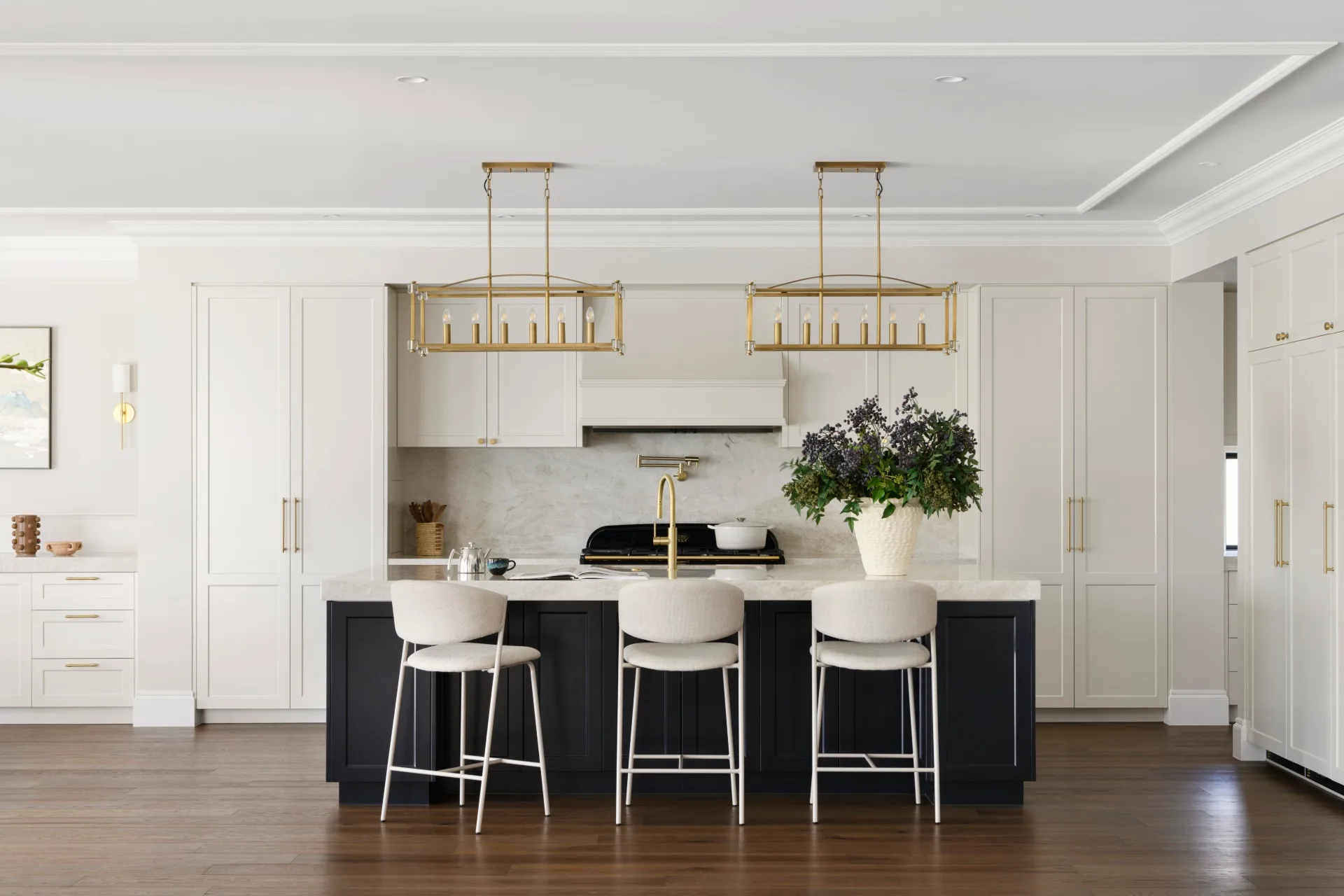 Modern kitchen with white cabinets, black island, gold accents, wooden floor, and two modern pendant lights.