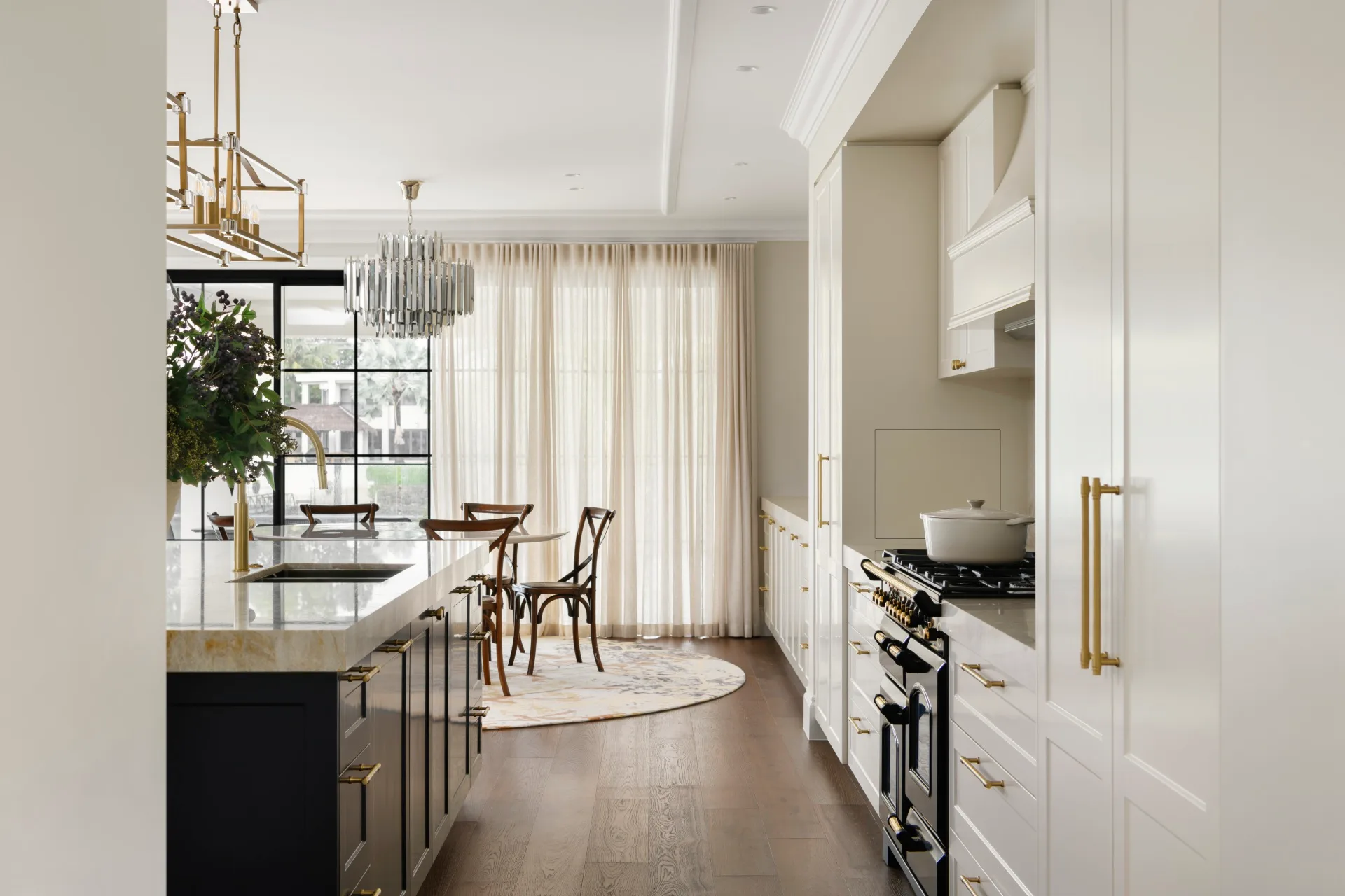 Modern kitchen with white cabinetry, large island, gold accents, chandelier, and wood floor.