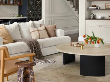 Modern living room with beige sofa, wooden coffee table, shelves, staircase, and ceiling fan.
