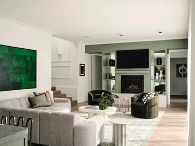 Bright living room with green accents, plush sofas, plant decor, and a fireplace beneath a wall-mounted TV.