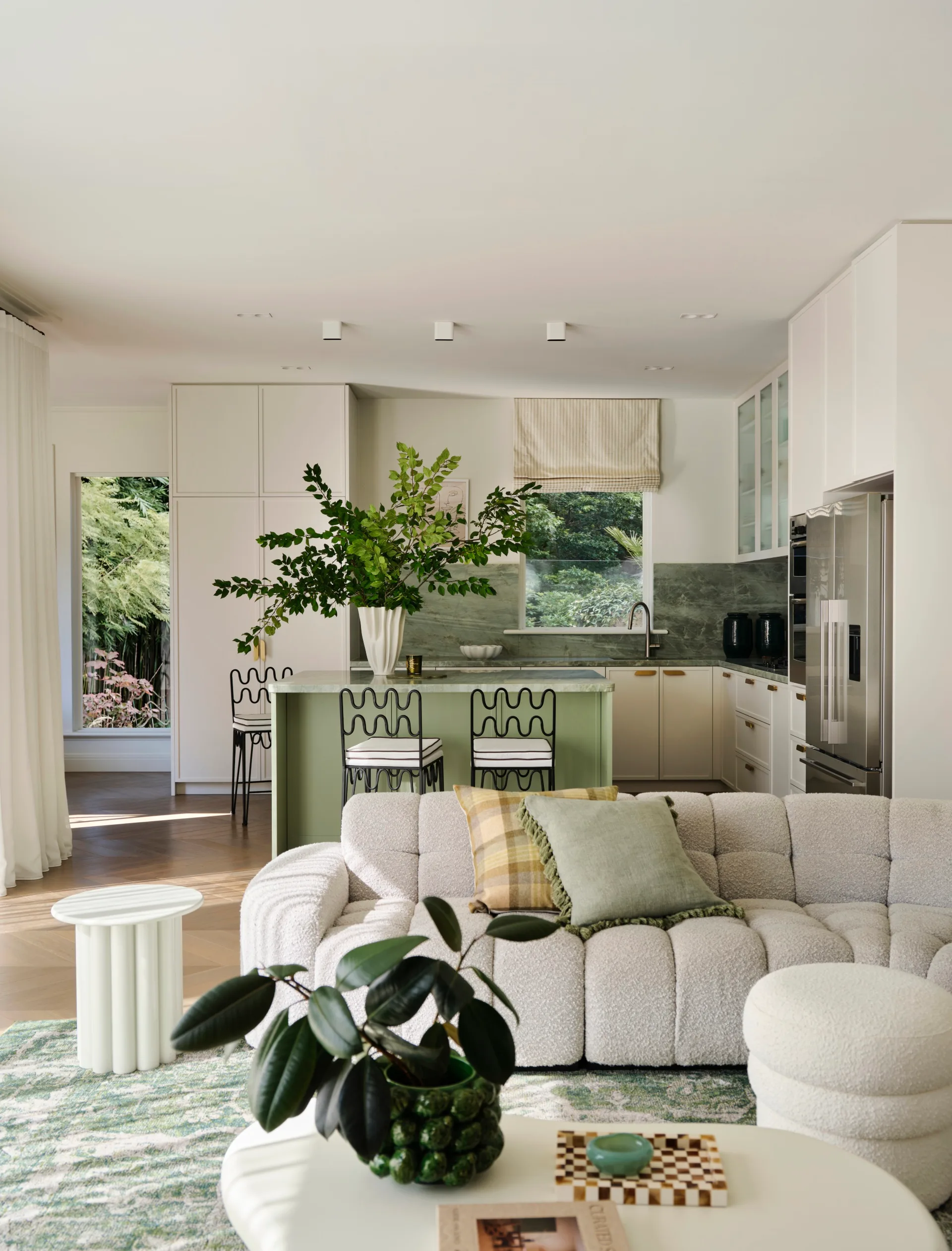Modern open-plan kitchen and living room with a white sofa, green accents, and a decorative plant on a coffee table.