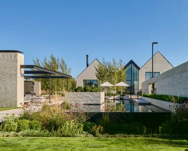 Modern building with large glass windows, surrounded by landscaped garden and pool, under a clear blue sky. garden.
