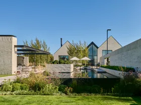 Modern building with large glass windows, surrounded by landscaped garden and pool, under a clear blue sky. garden.