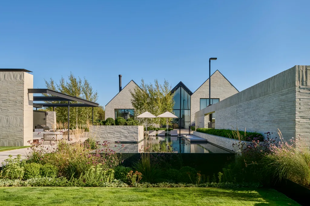 Modern building with large glass windows, surrounded by landscaped garden and pool, under a clear blue sky. garden.