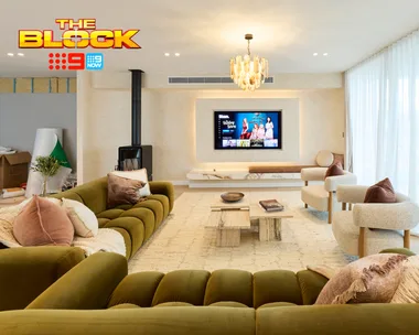 Luxurious living room from "The Block" with green sofa, armchairs, TV, and chandelier under soft lighting.