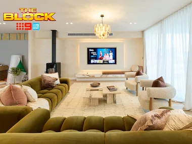 Luxurious living room from "The Block" with green sofa, armchairs, TV, and chandelier under soft lighting.
