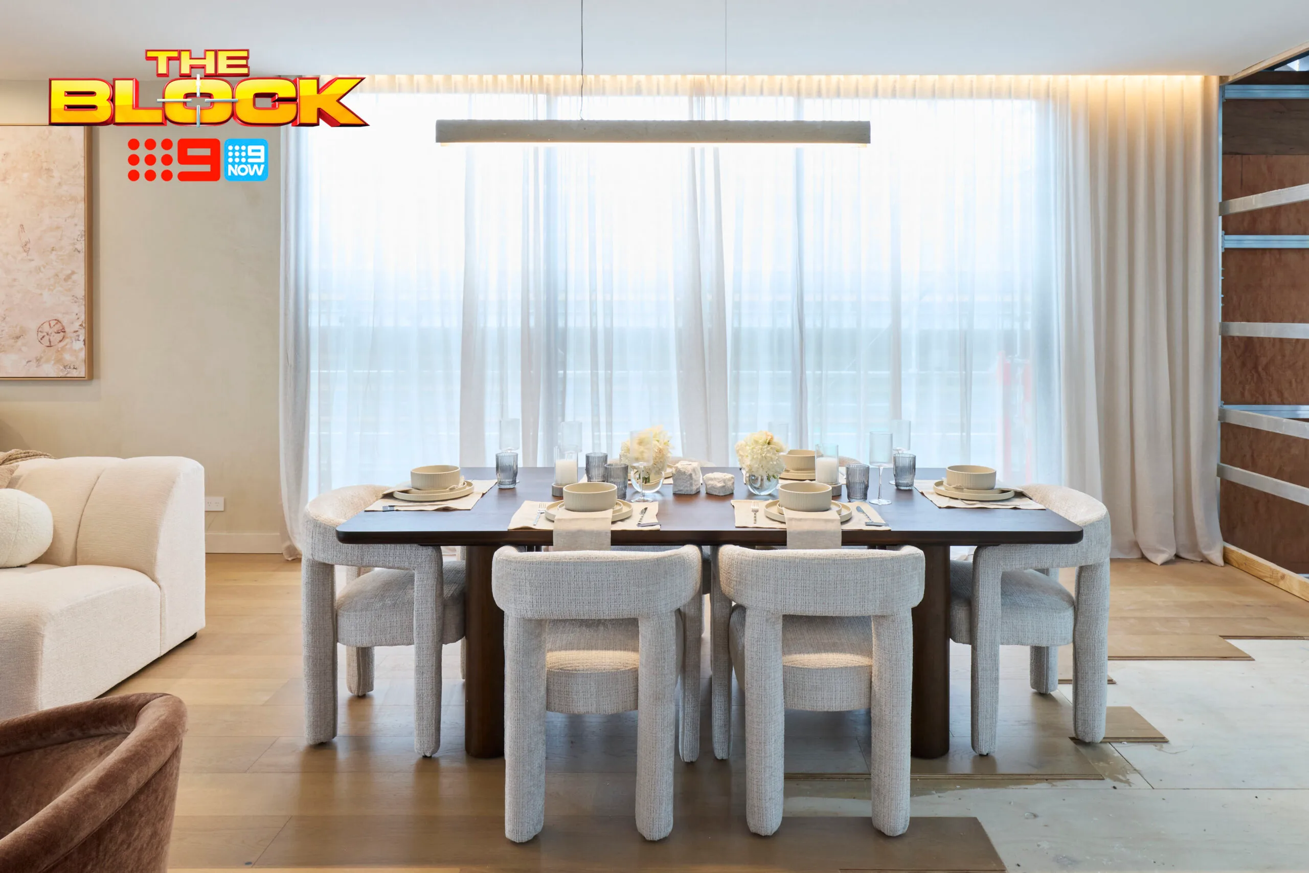 Modern dining room with a dark wood table, cream chairs, and tableware set for six under soft lighting.