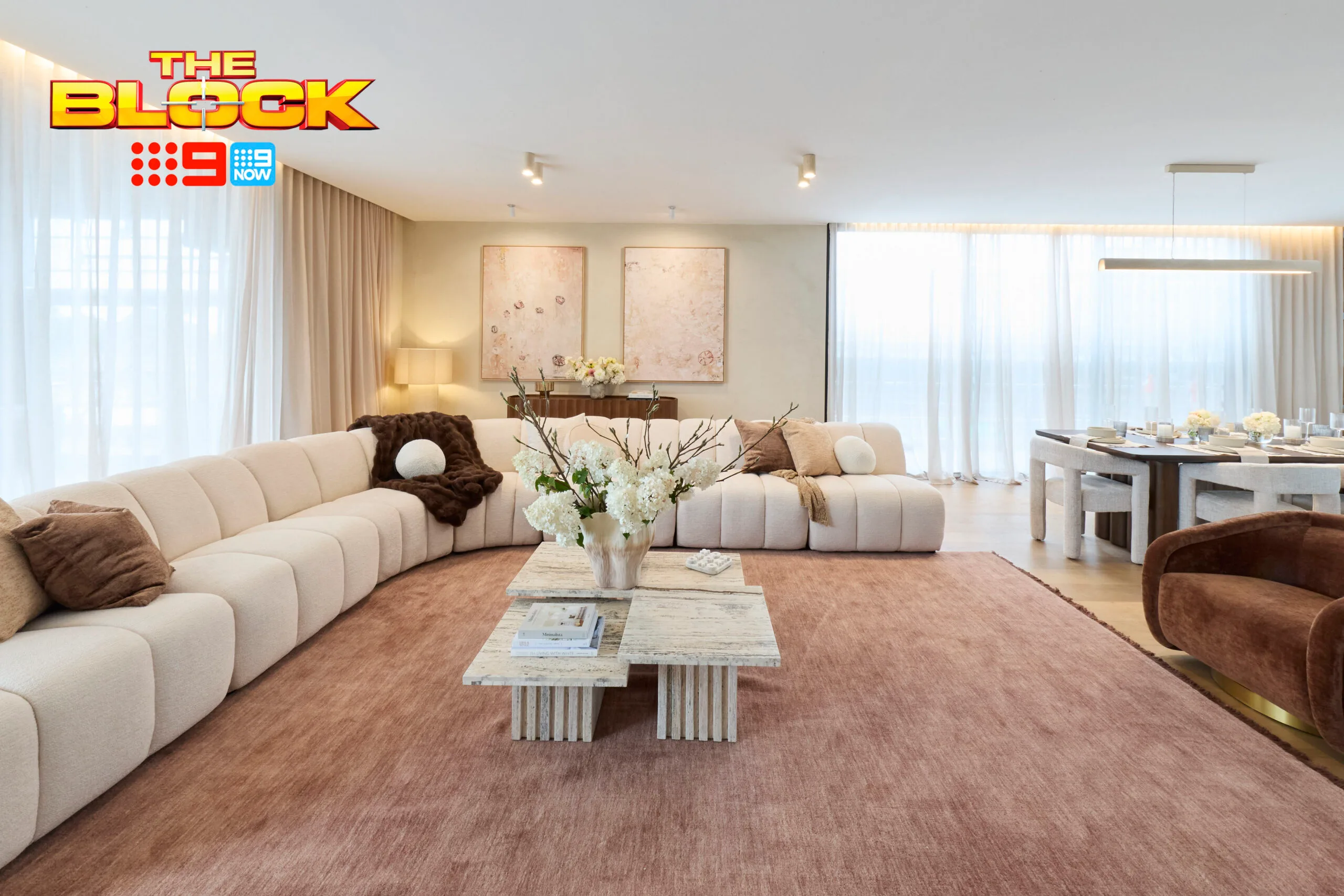 Modern living room from "The Block" show with cream sofas, pink rug, and a stylish coffee table arrangement.