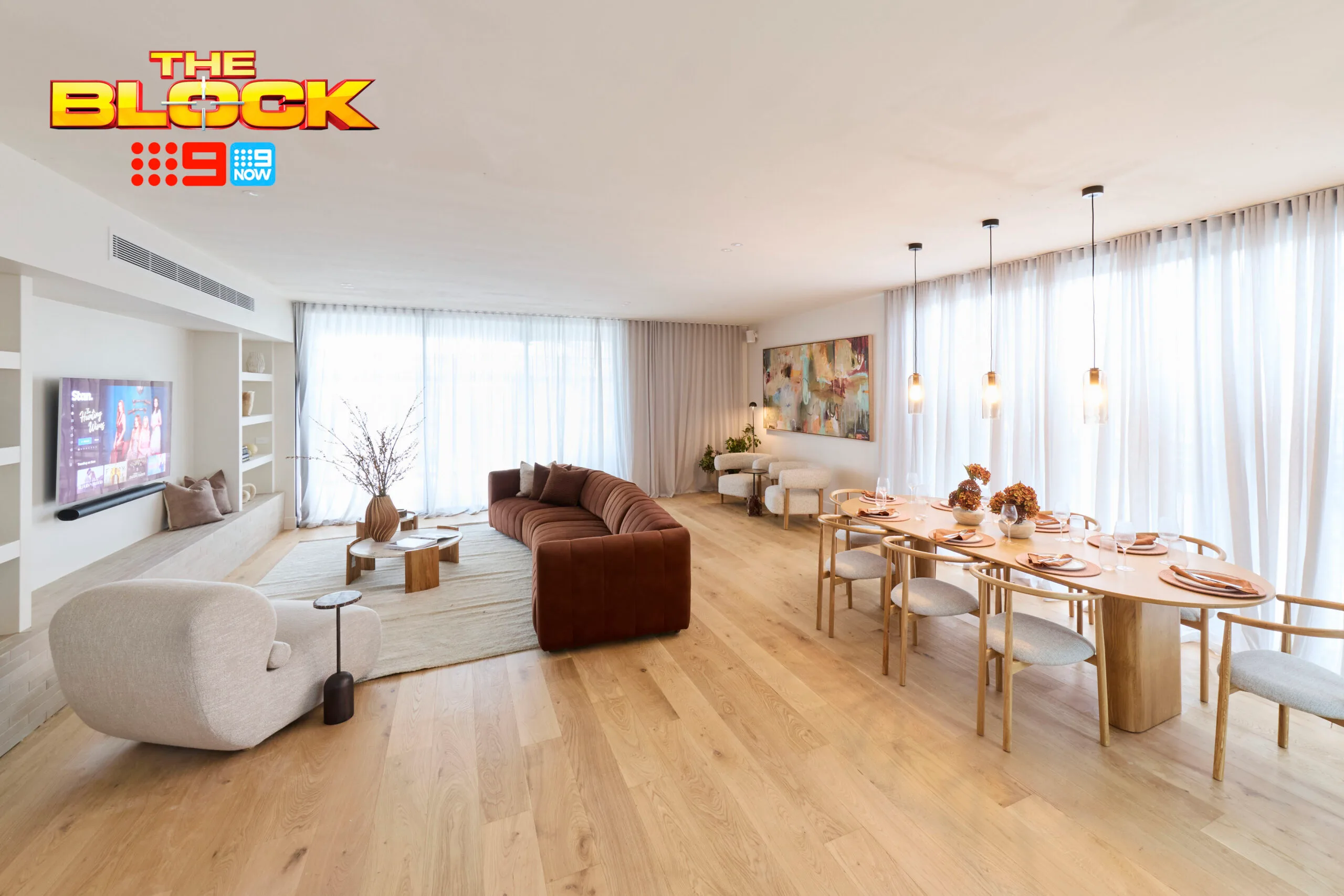 Living room and dining area with modern decor, a TV, brown sofa, art piece, and wooden flooring from "The Block" show.