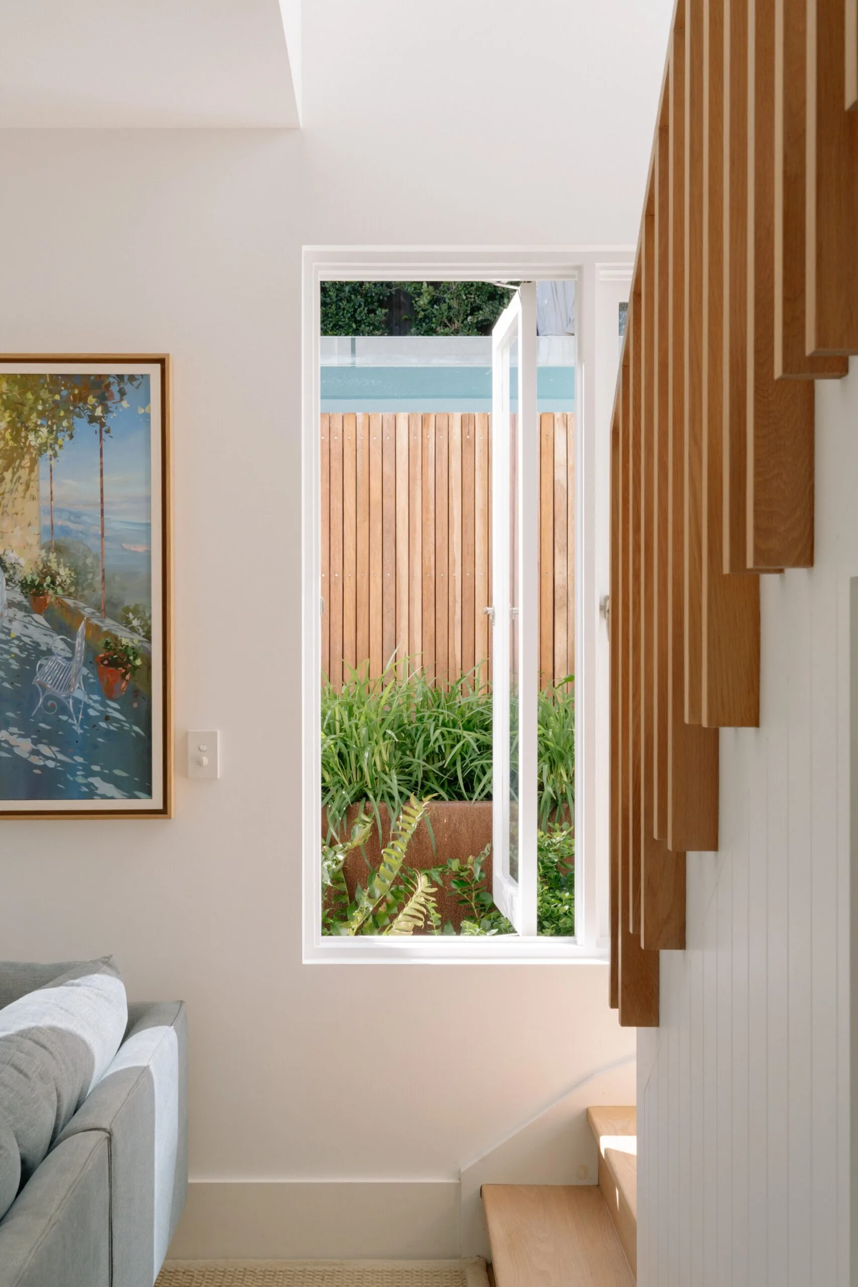 Bright interior with stairs, open window, garden view, and framed painting. Cozy and inviting space.