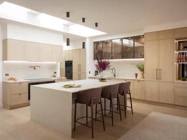 Contemporary kitchen with large island, bar stools, wooden cabinets, and skylight.