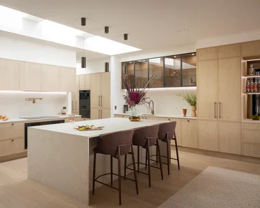 Contemporary kitchen with large island, bar stools, wooden cabinets, and skylight.