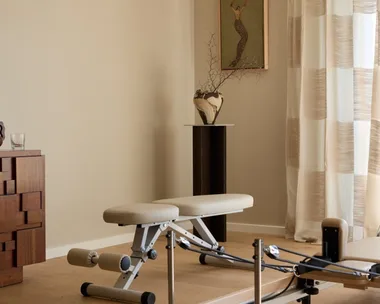Contemporary home gym with a reformer machine, wooden floor, and abstract art on the wall.
