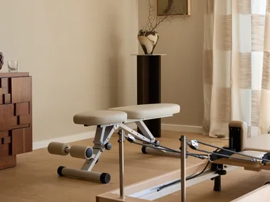 Contemporary home gym with a reformer machine, wooden floor, and abstract art on the wall.