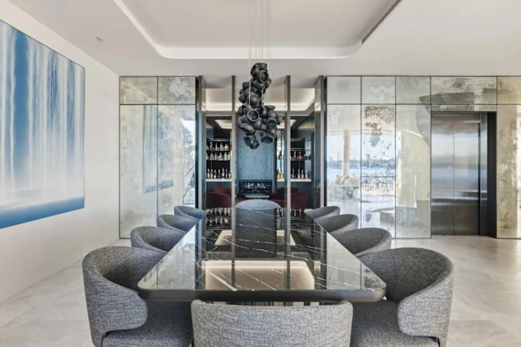 Luxurious dining room with a long black marble table, elegant grey chairs, modern chandelier, and mirrored walls.