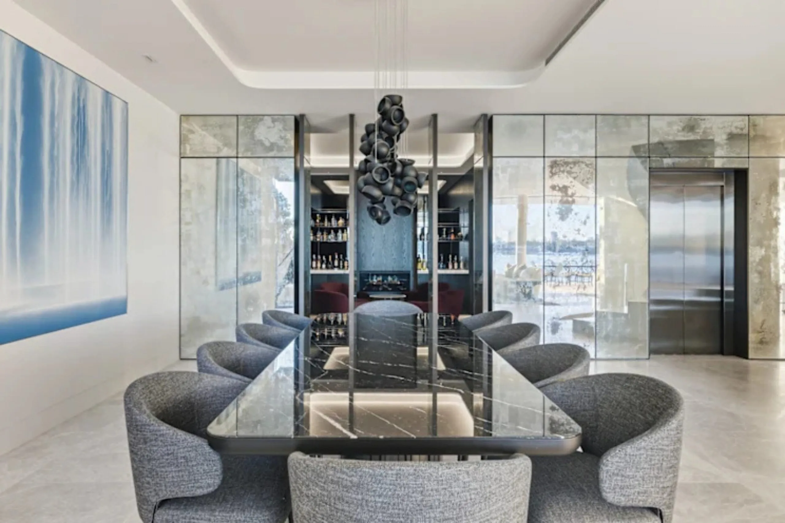 Luxurious dining room with a long black marble table, elegant grey chairs, modern chandelier, and mirrored walls.