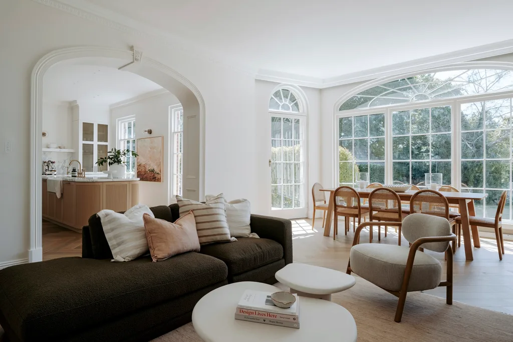 A bright living room with a sofa, armchair, coffee table, and dining area set by large windows.