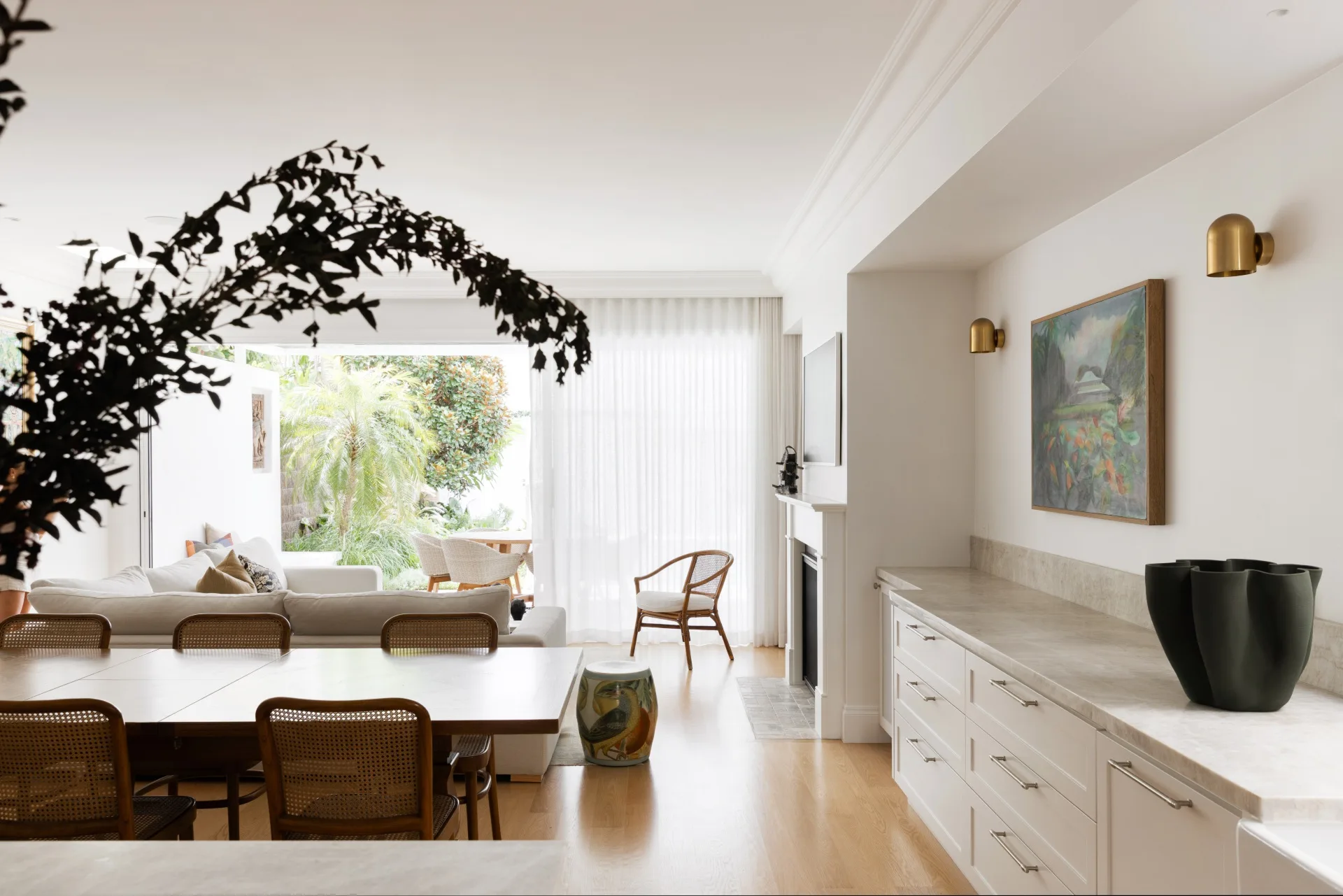 Modern living room with light decor, large windows, wooden furniture, and a view of a lush garden.