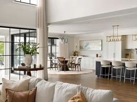 Modern open-plan living room and kitchen with large windows, light decor, and a dining area.