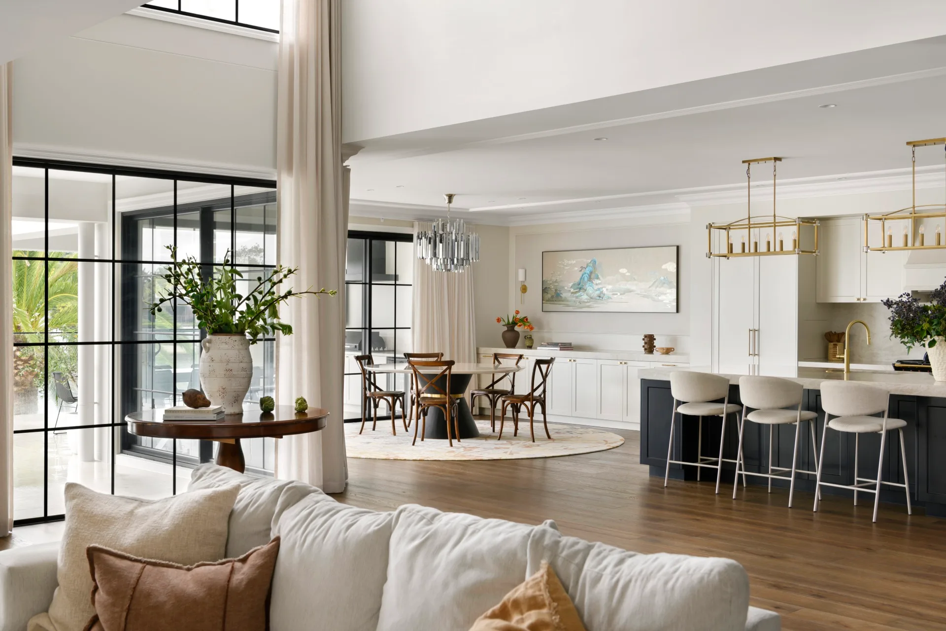 Modern open-plan living room and kitchen with large windows, light decor, and a dining area.