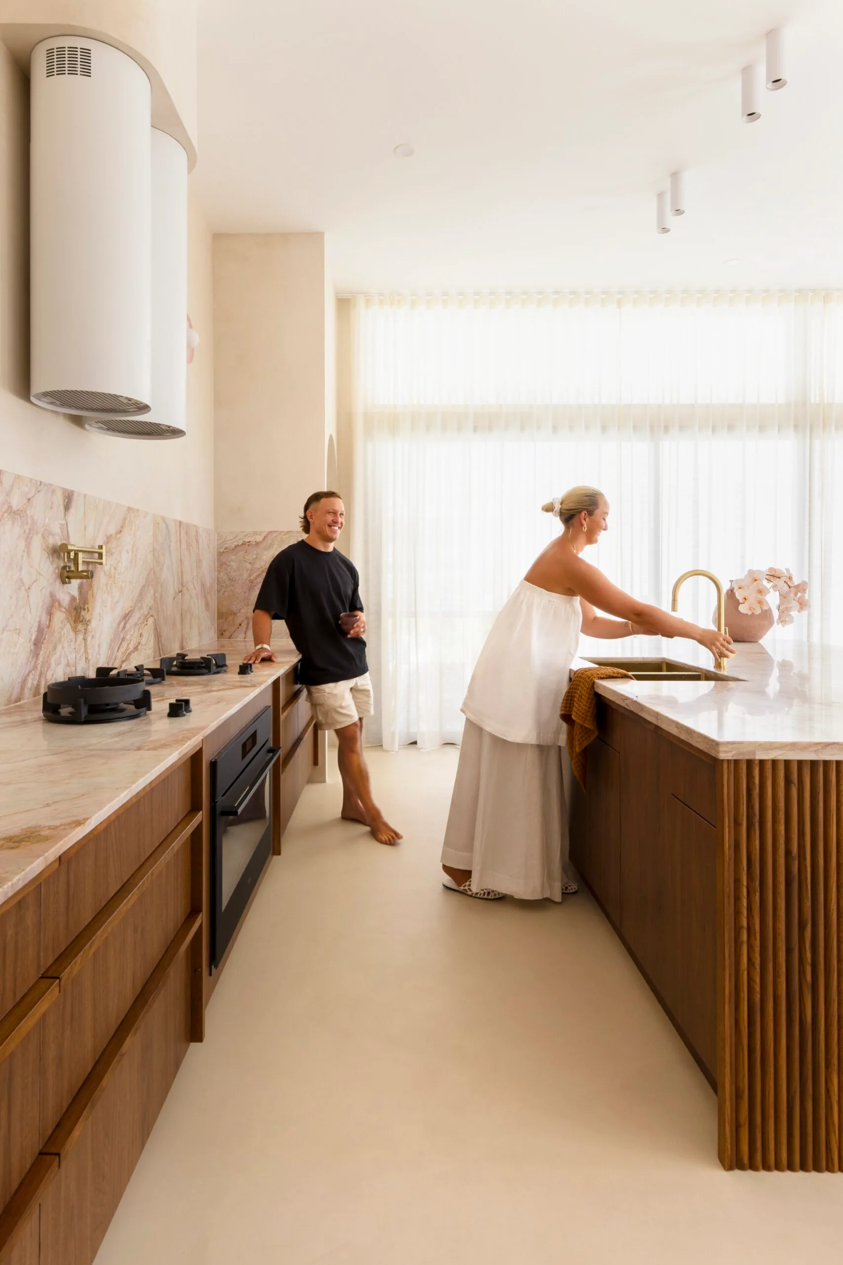 A man and woman enjoying their modern kitchen, with marble countertops and wooden cabinetry.