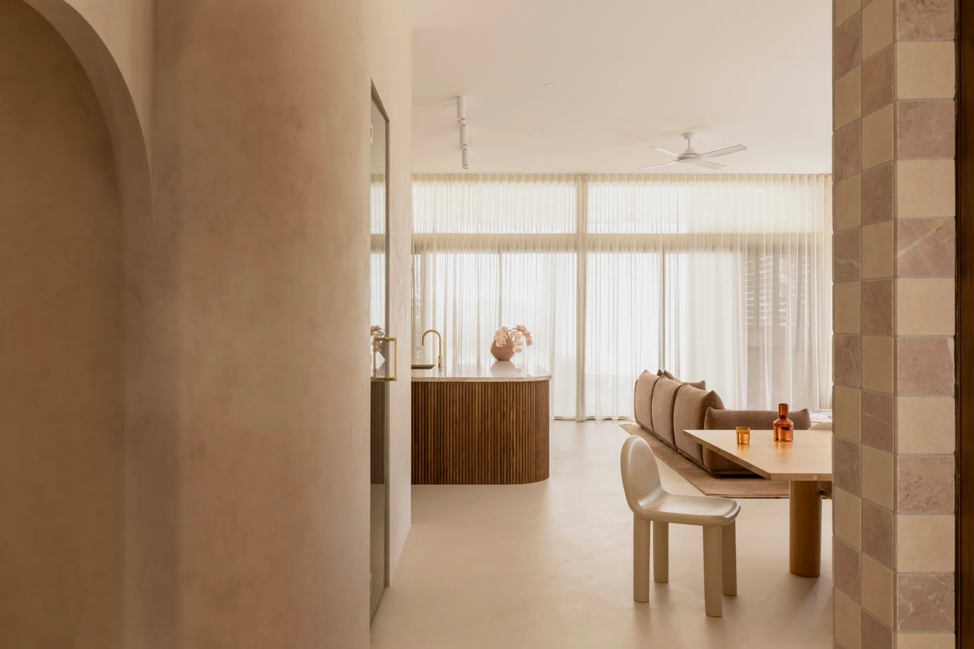 Modern interior with neutral tones, featuring a round dining table with a white chair, a brown sofa, and sheer curtains.