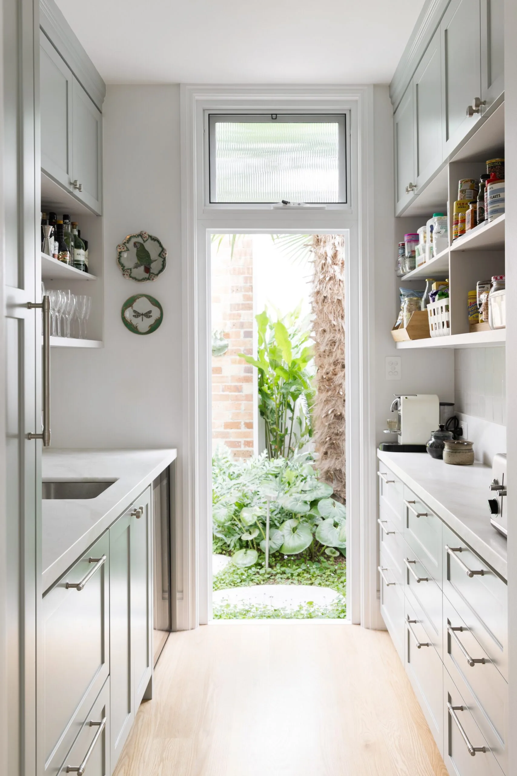 Narrow kitchen with mint cabinets, open shelving, and door leading to a lush garden.