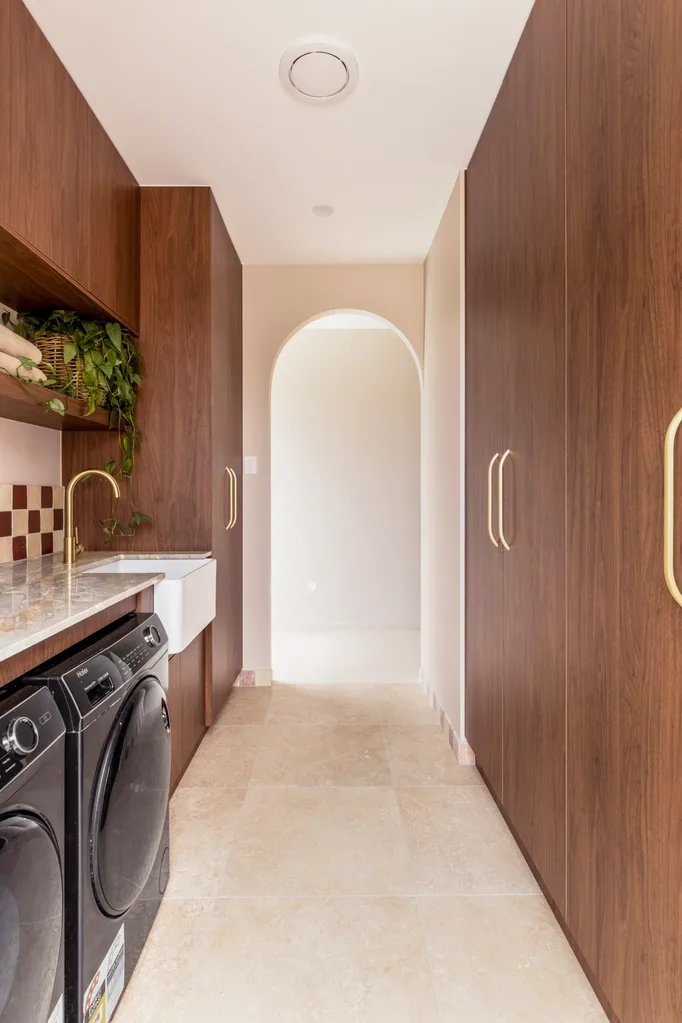 Modern laundry room with wood cabinets, a black washer and dryer, and a plant on a shelf, leading to an arched doorway.