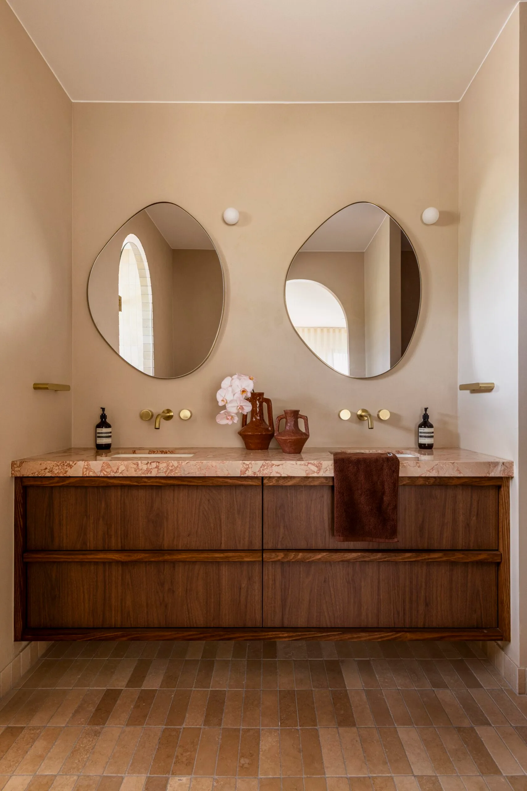 Dual vanity with unique mirrors, marble countertop, and wood cabinetry in a beige bathroom.