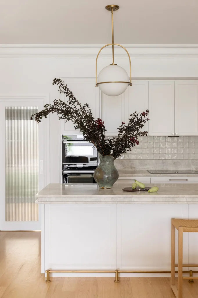 Elegant kitchen with a white island, large vase with branches, modern pendant light, and fresh zucchini on the counter.