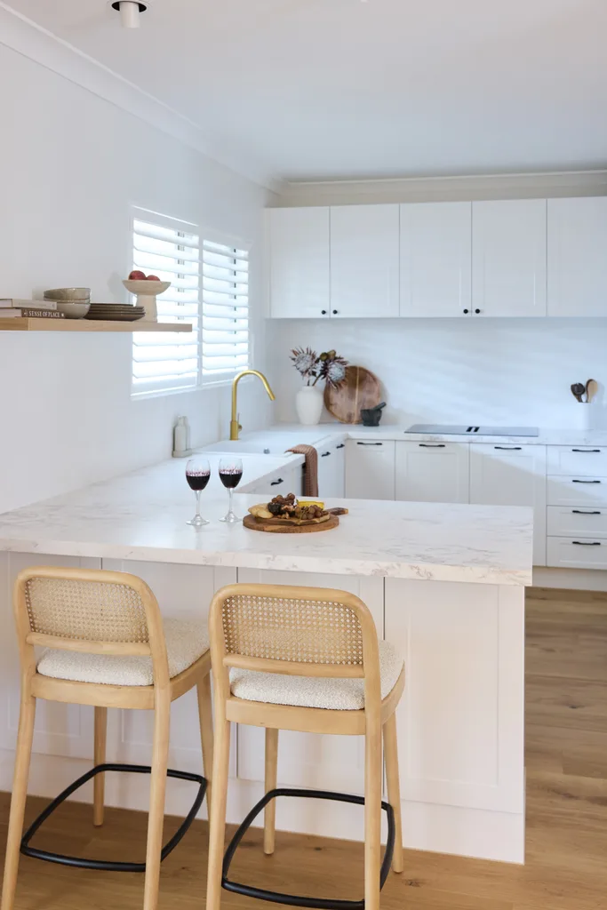 Modern kitchen with white cabinets, marble countertop, two wooden stools, a charcuterie board, and two glasses of red wine.