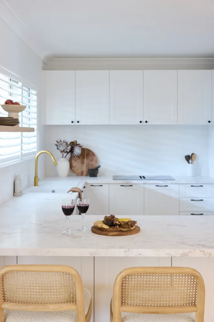 Modern kitchen with white cabinets, a marble countertop, two chairs; two wine glasses and a platter with grapes.