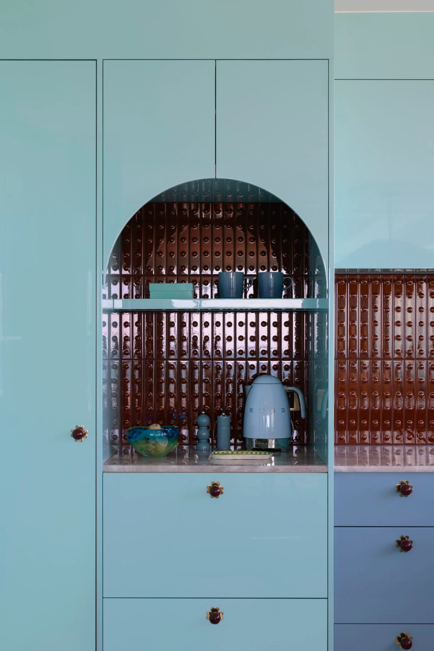 Aqua blue kitchen cabinetry with arch alcove, copper backsplash, and retro blue kettle.