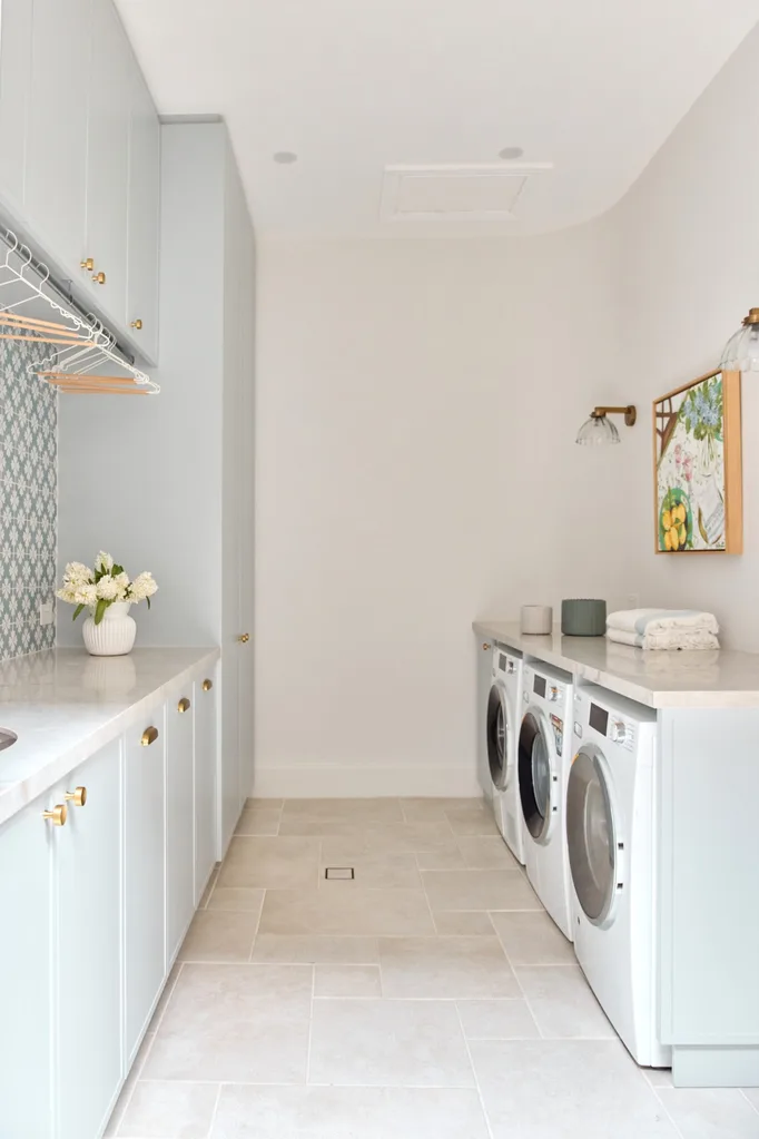 Modern laundry room with light blue cabinets, white countertops, front-load washers, and decorative wall art.