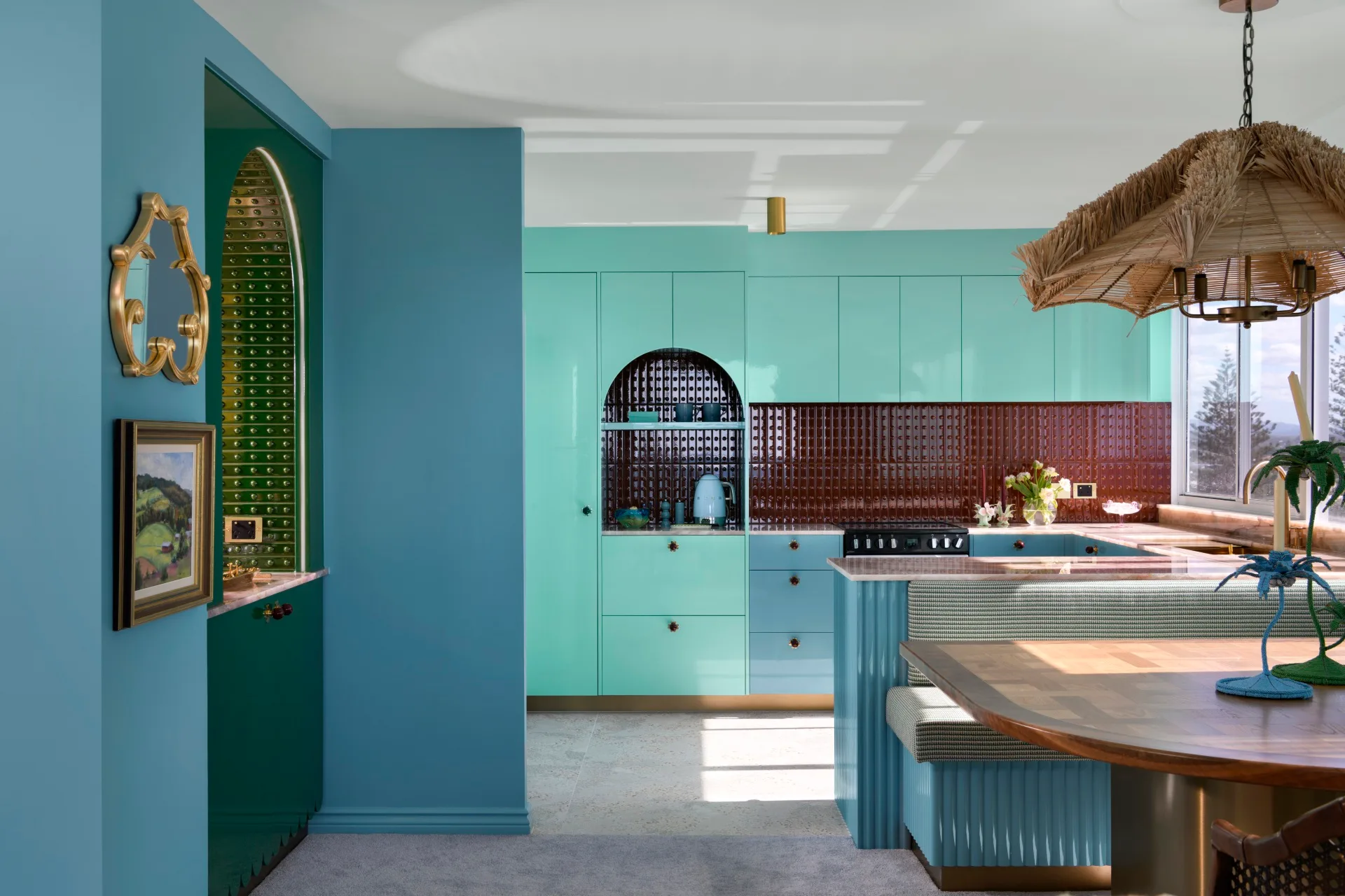 A vibrant kitchen with teal cabinets, red-tiled backsplash, arched niche, tropical decor, and large window.