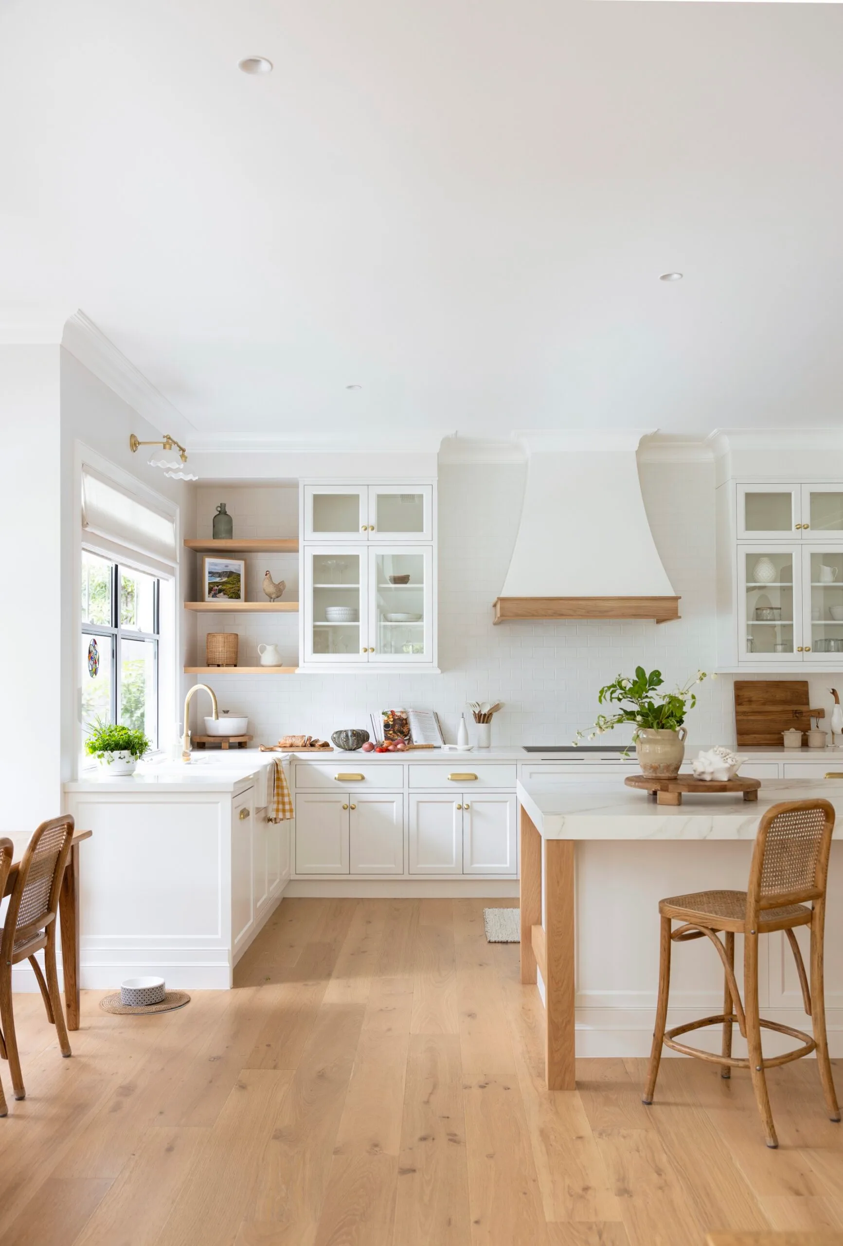 Bright modern kitchen with white cabinets, wooden floor, island with chairs, and plants on countertops.