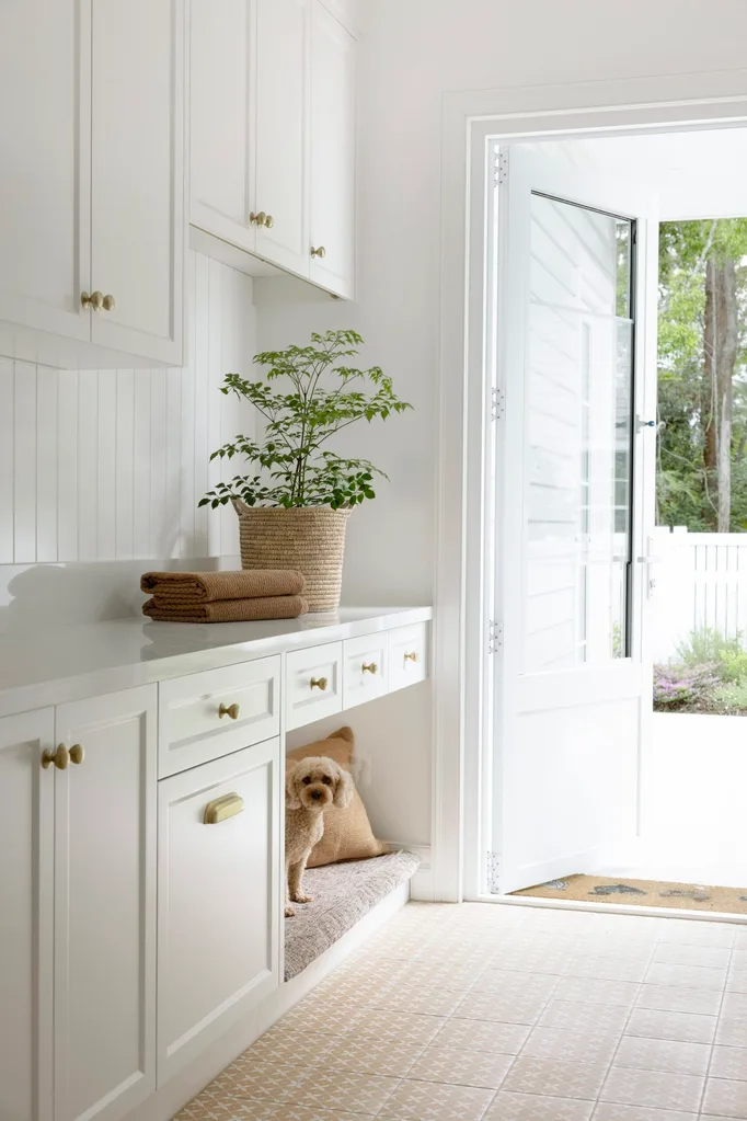 Cozy laundry room with open door, leafy plant, stacked towels, and a small dog in a nook under the cabinets.