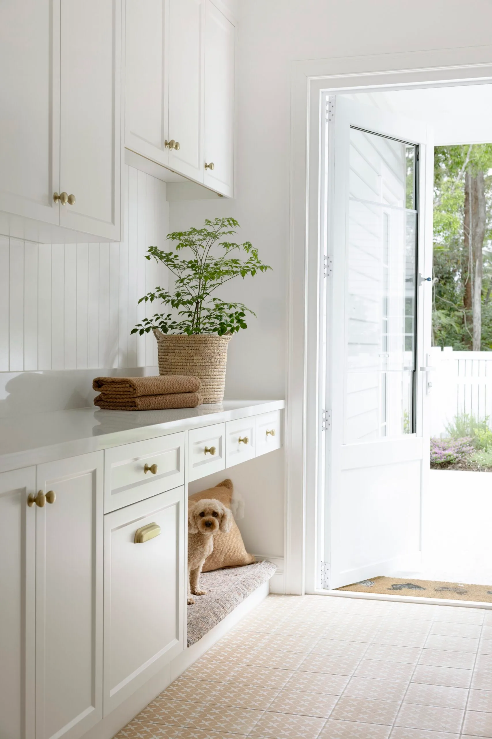 Cozy laundry room with open door, leafy plant, stacked towels, and a small dog in a nook under the cabinets.