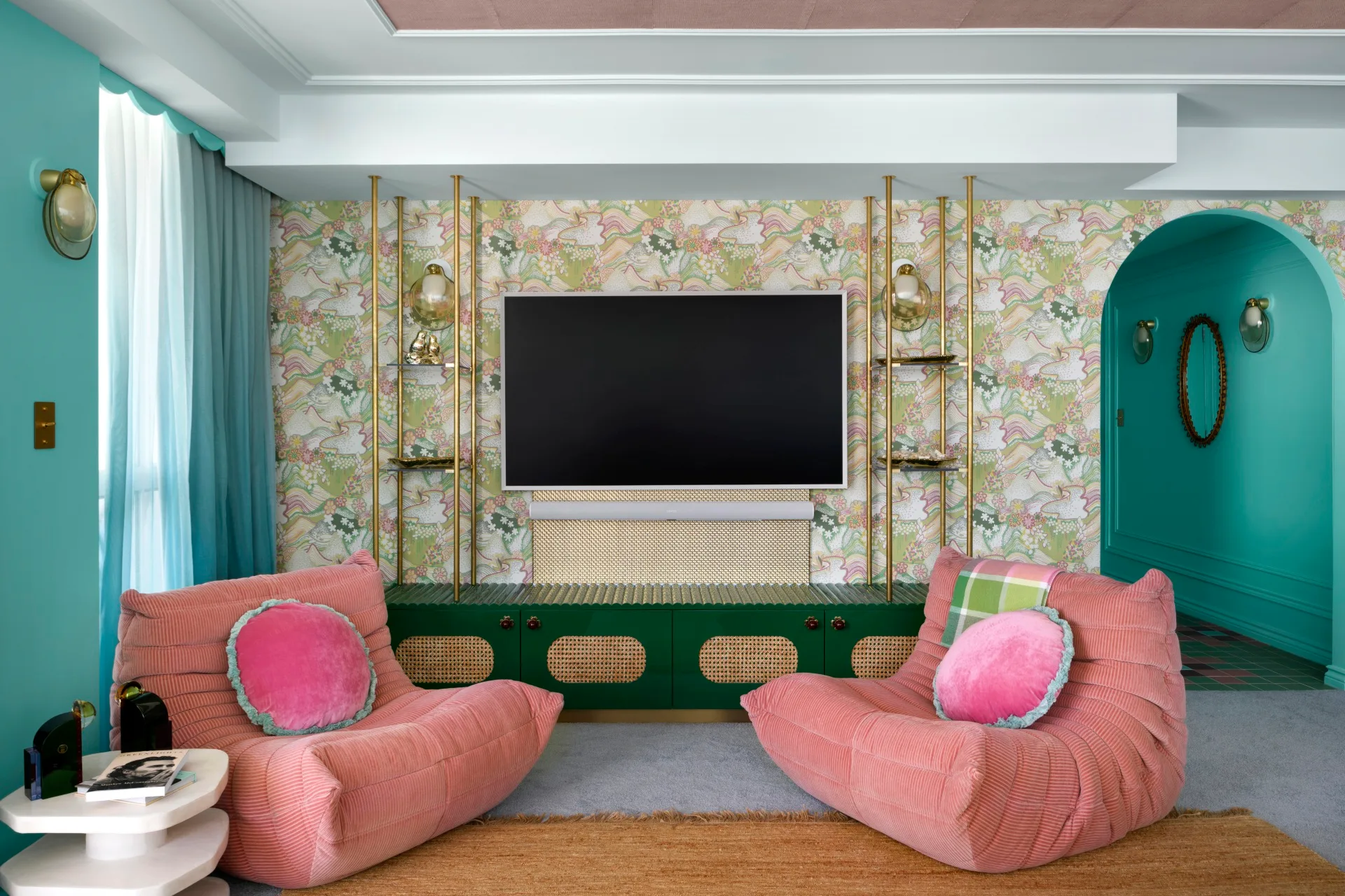 Living room with pink chairs, floral wallpaper, teal walls, and a TV on a decorative cabinet.