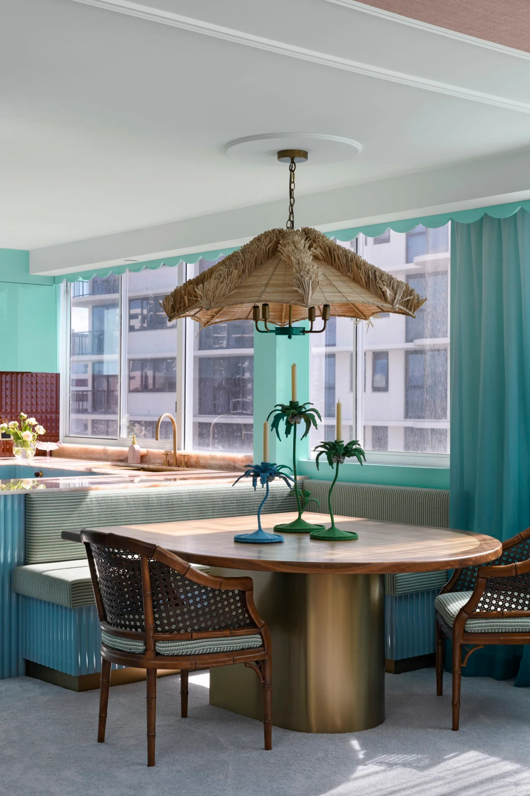 Dining room with rattan chairs, round table, palm tree candles, and a straw pendant light in a tropical decor theme.
