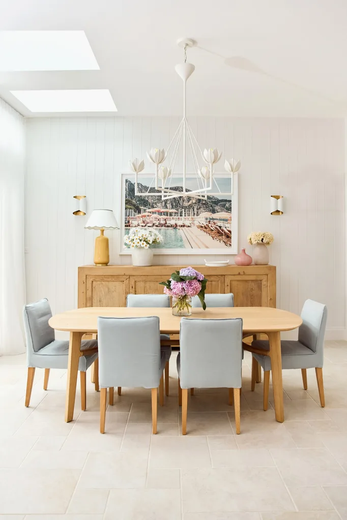Dining room with wooden table, six blue chairs, floral centerpiece, wall art, and light fixture.