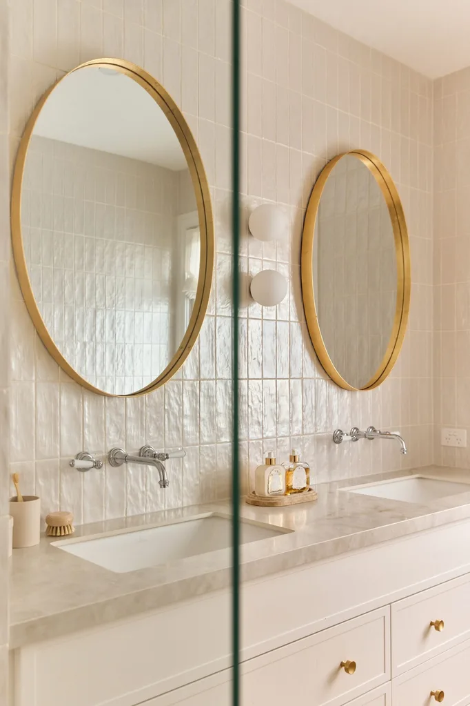 Elegant bathroom with two round mirrors, dual sinks, and gold accents on the faucets and mirror frames.