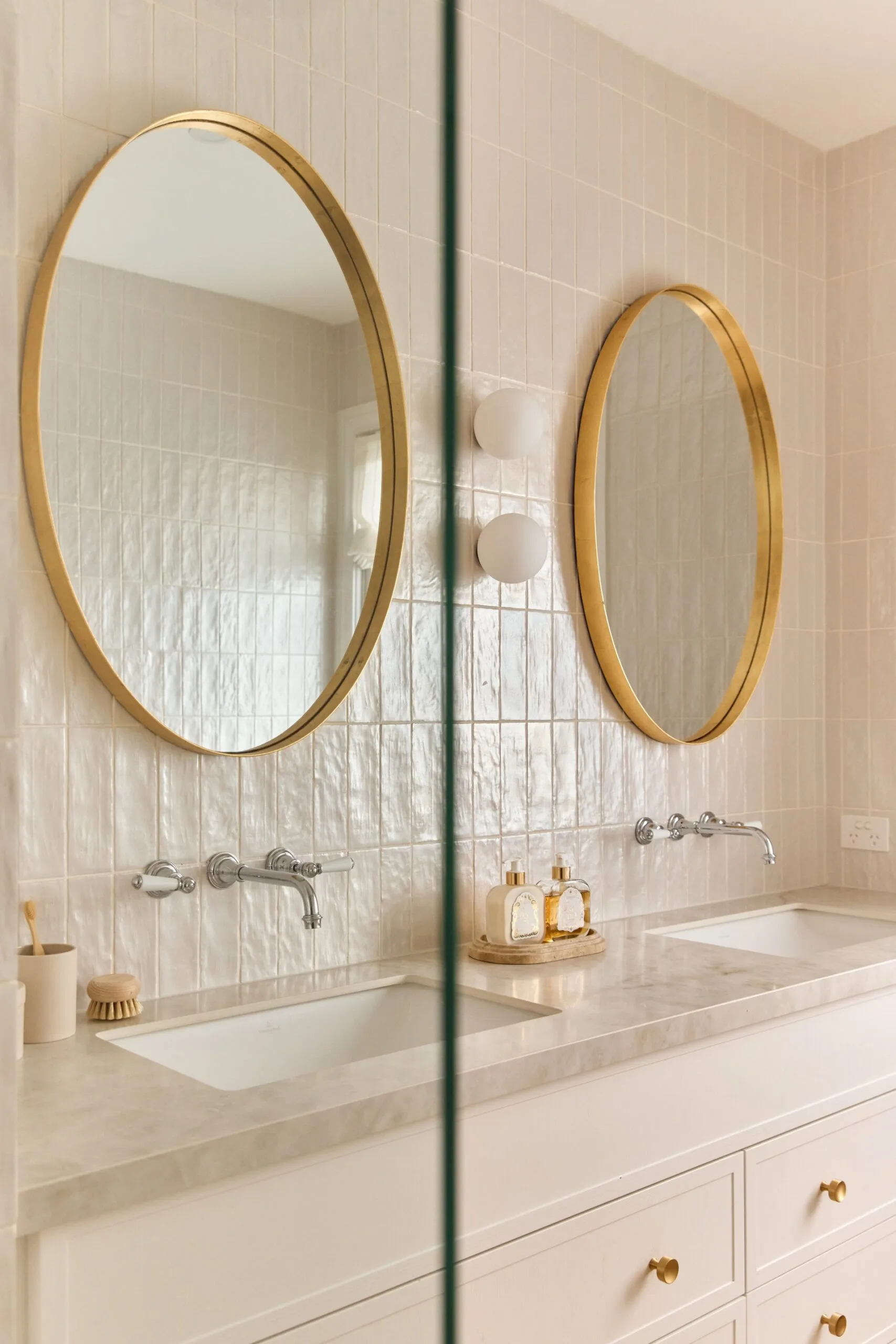 Elegant bathroom with two round mirrors, dual sinks, and gold accents on the faucets and mirror frames.