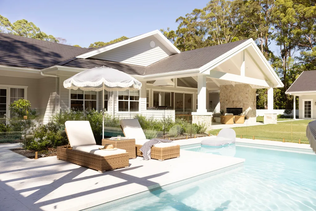 Luxurious backyard with a pool, sun loungers under an umbrella, and a modern house surrounded by lush greenery.