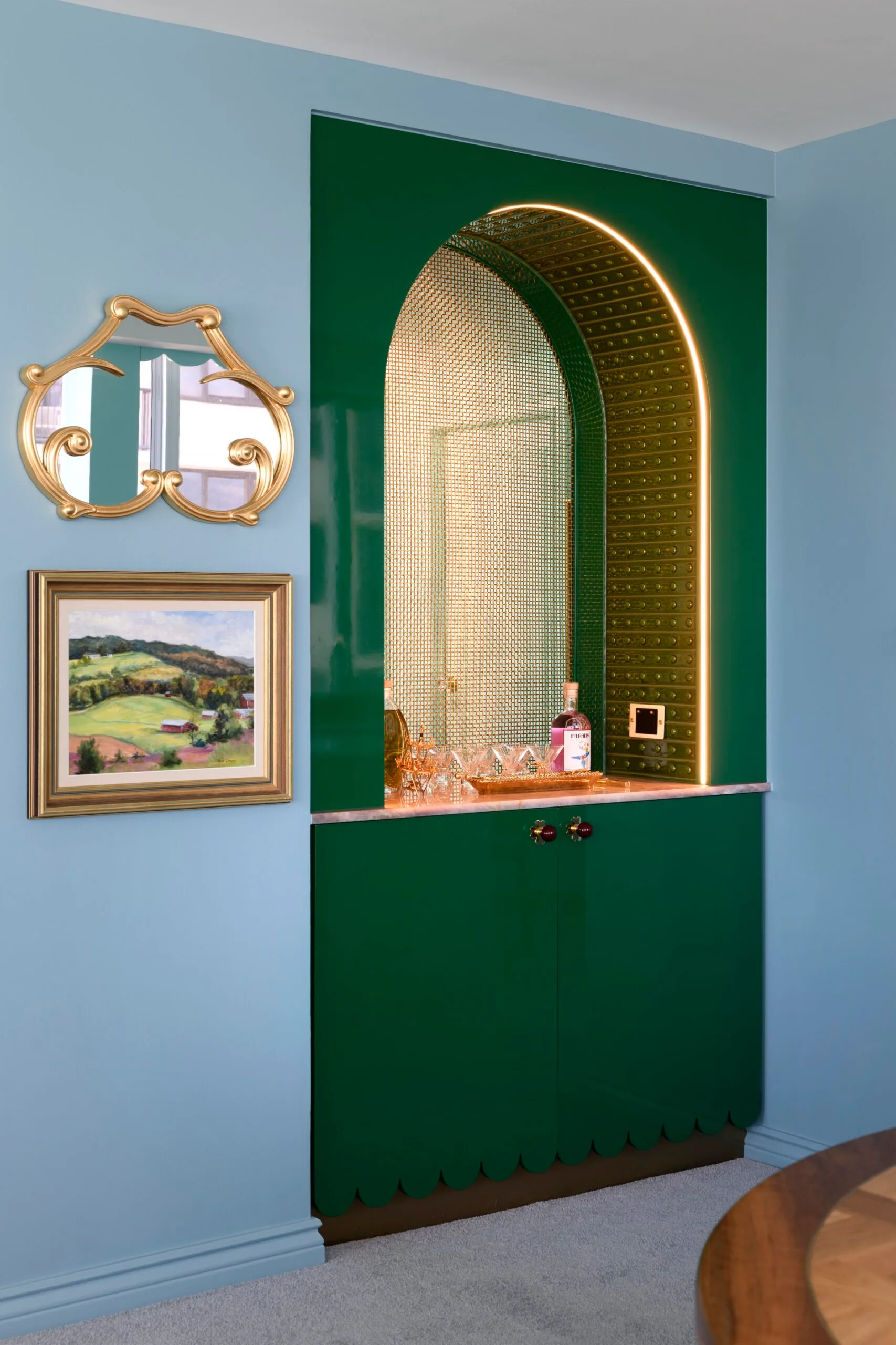 Elegant nook with green arch, gold mirror, and framed landscape painting on a light blue wall.