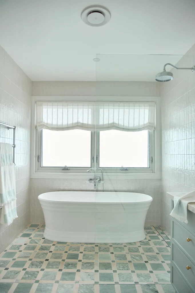 Bright bathroom with a freestanding bathtub, checkered floor tiles, large window, and overhead showerhead.