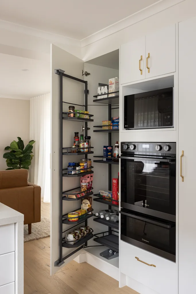 Open kitchen pantry with organized shelves, oven, microwave, and various food items.