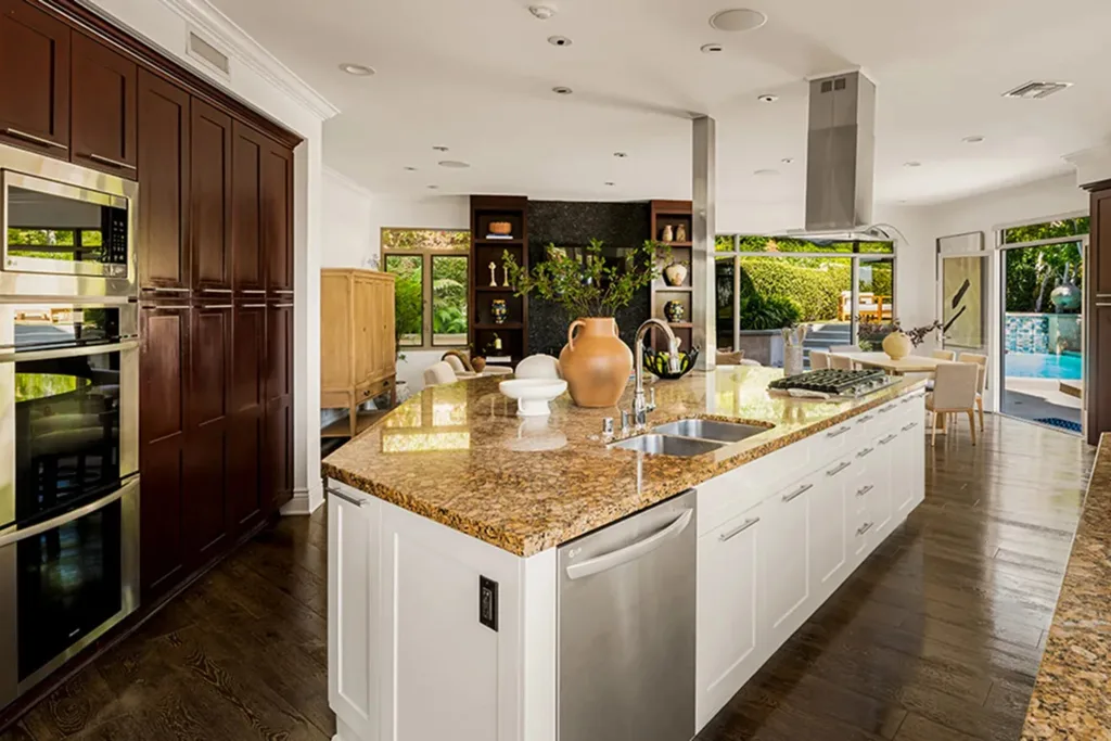 Modern kitchen with large granite island, stainless steel appliances, and view of a garden through wide windows. Dolly Parton's Hollywood Hills home.